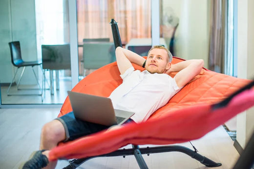 homme avec un ordinateur portable, les mains derrière la tête, se détendant et rêvant, allongé sur un hamac dans un bureau